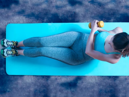 A woman is laying on a blue mat with a dumbbell.