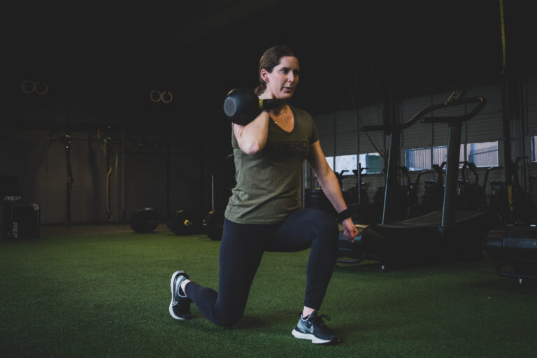 A woman squatting with a dumbbell in a gym.