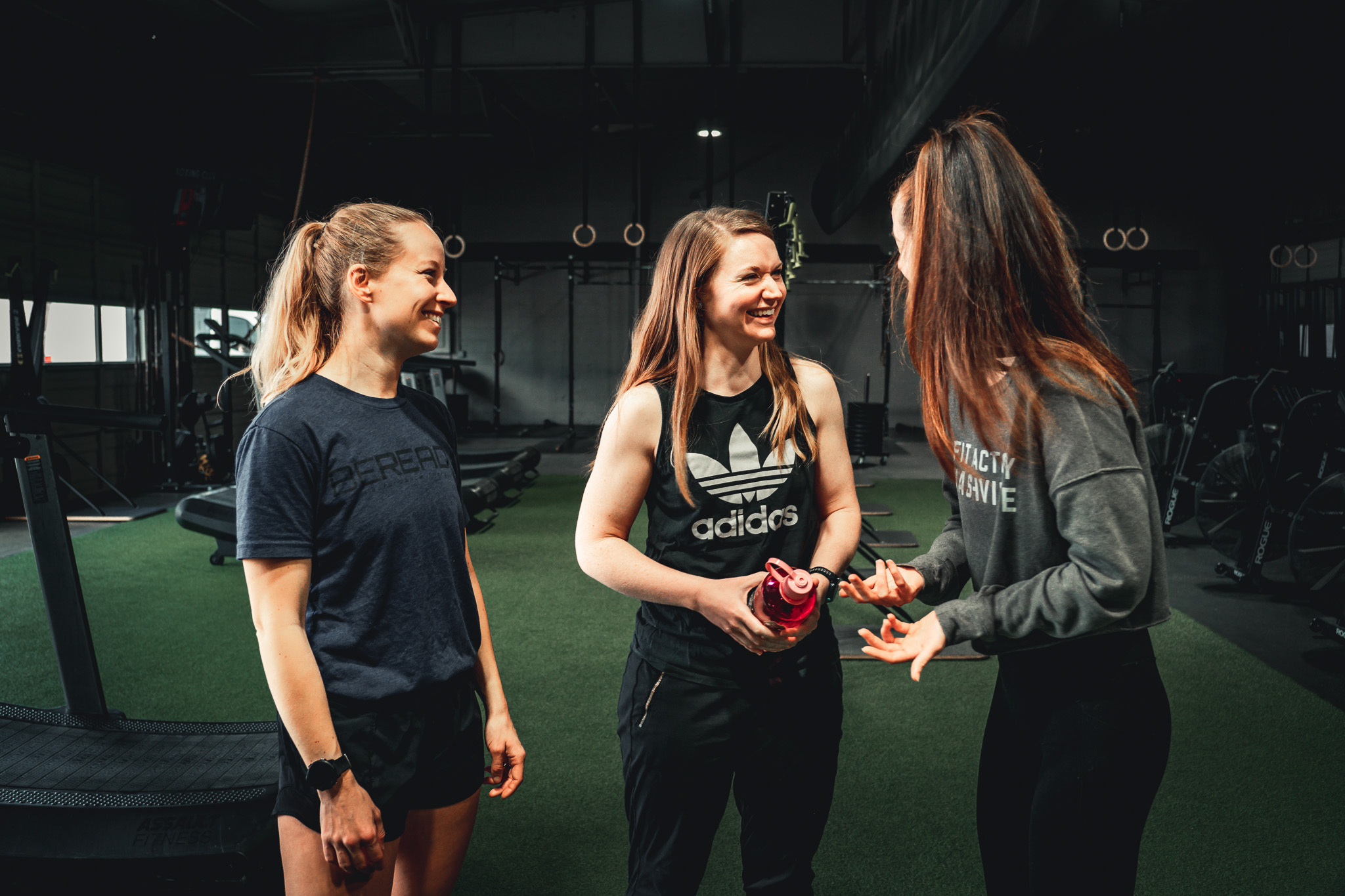 Three women in a gym talking to each other.