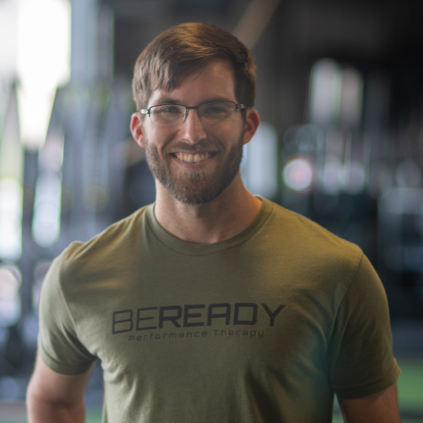A man in a green t - shirt smiles in front of a gym.