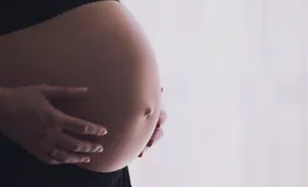 A pregnant woman with her hands on her stomach.