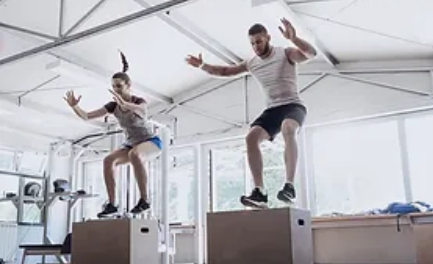 Two people doing box jumps in a gym.